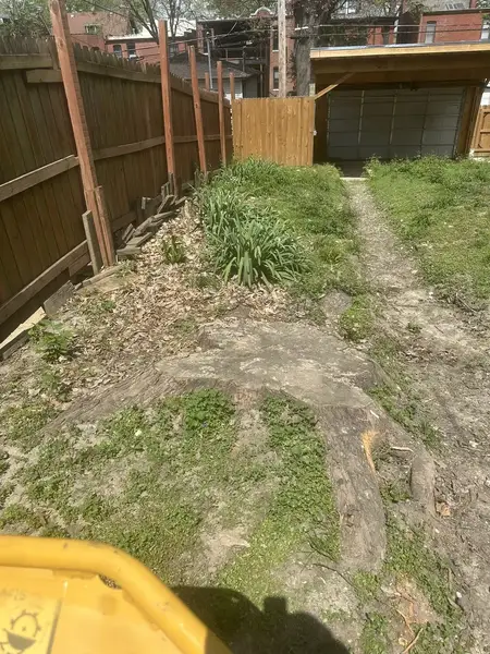 Stump grinder working along a wooden privacy fence