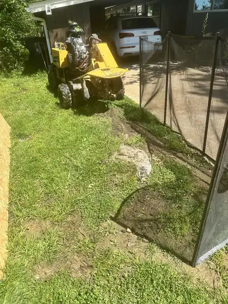 Stump grinder working behind a safety screen near a carport