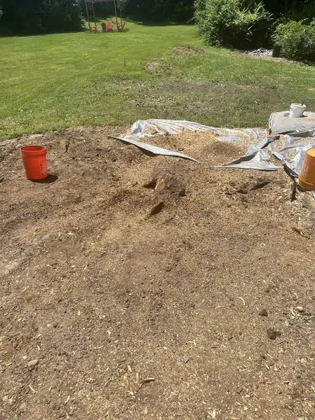 Patch of soil with a tarp and bucket after stump grinding